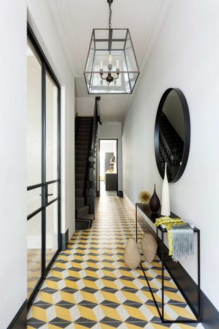 white entryway with yellow and black floor tiles, black mirror, console, crittall doors, lantern