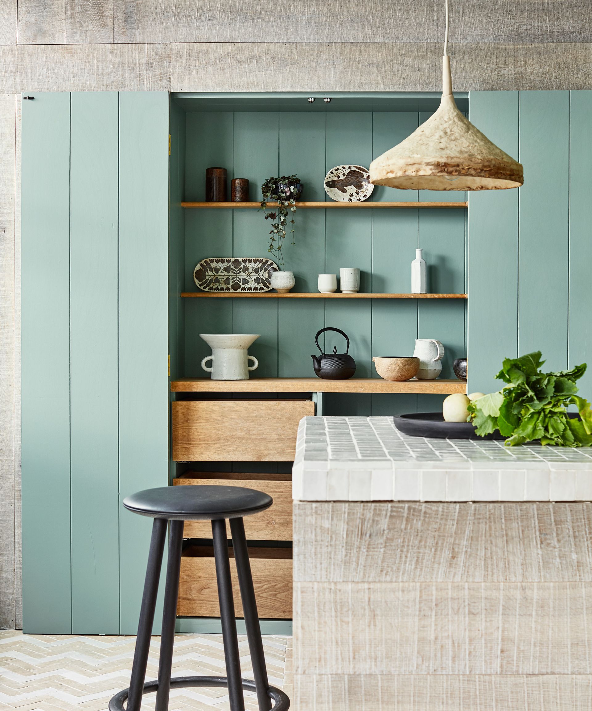 Floor to celing sea green kitchen cabinets with wooden shelving inside, and a white kitchen island with black bar stool.