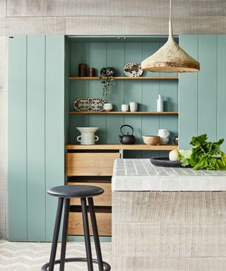 A neutral kitchen island in front of green kitchen wall panels and a hidden storage space