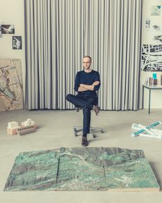 a photo of Simon Kretz seated with a few urban design models and, left, sketches and photographs of a Lake Lucerne house he completed in 2012 for his first practice