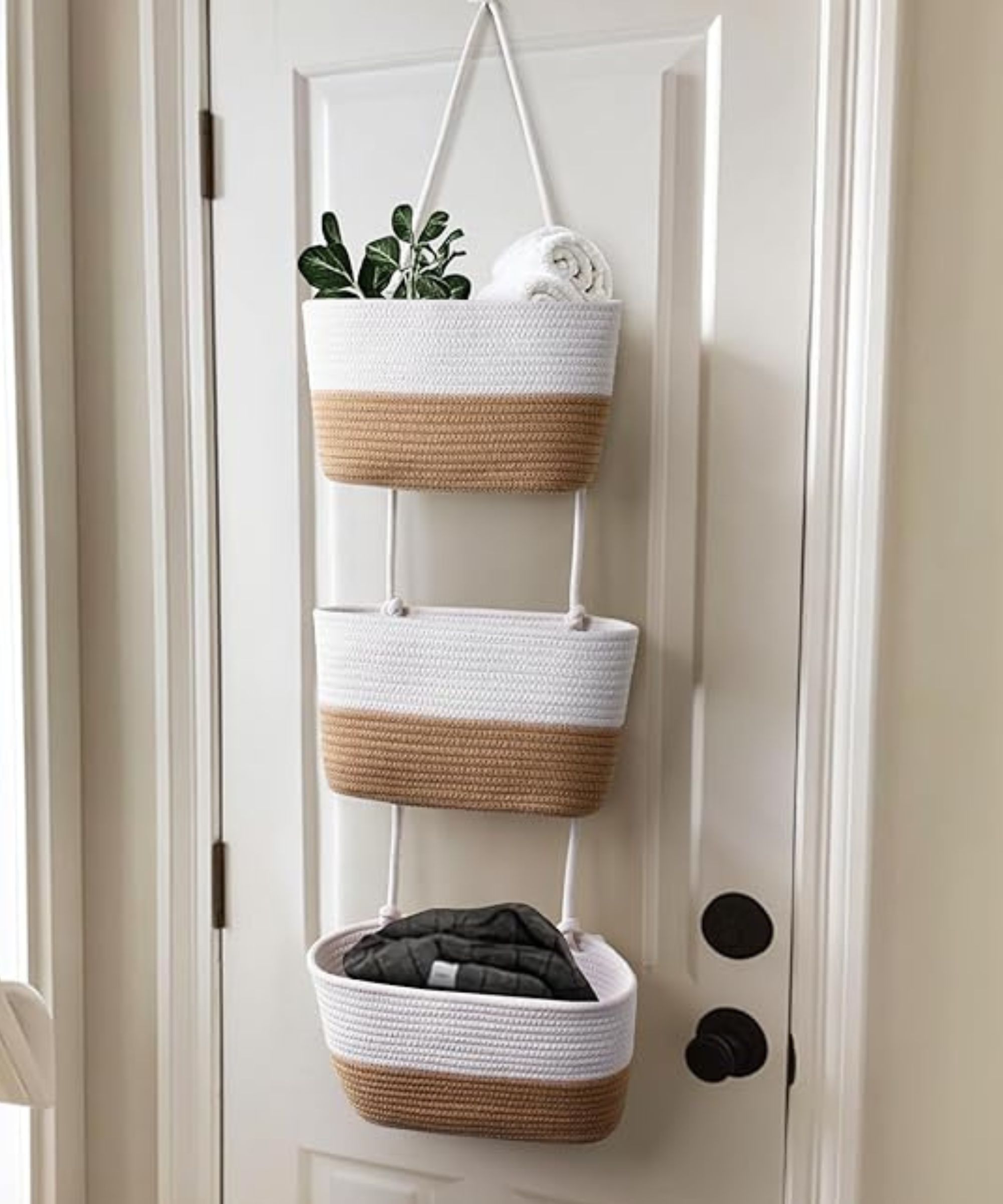 Three-tier over-the-door cotton rope basket storage. The baskets are light brown on the lower half, and white on the top half. The item is pictured in situ on a white internal door with black hardware