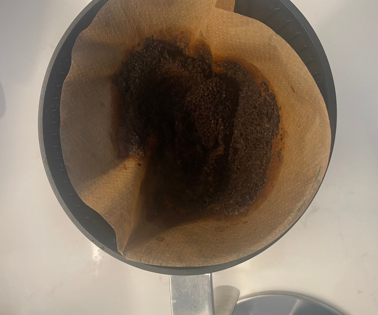 A close up of a used coffee filter with wet coffee grounds inside.