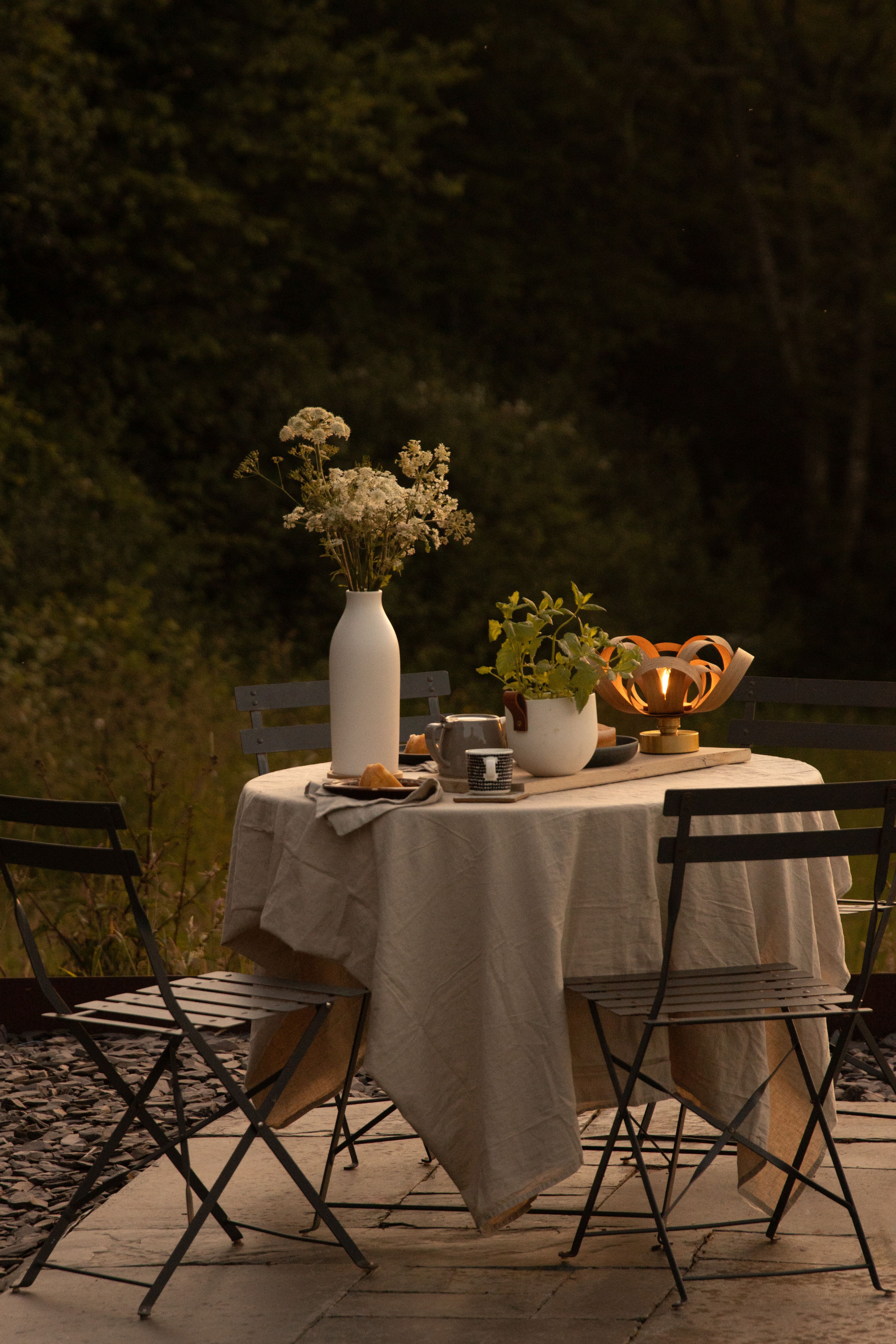 An outdoor dining setup with a singular wooden table lamp on it