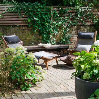 garden with plants on brick wall and wooden chair and potted plants