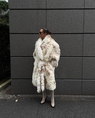 Woman wearing cream faux fur coat and matching ivory leather knee-high boots.