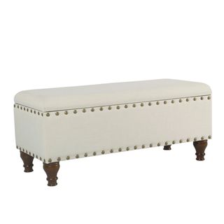 A cream storage ottoman with brass tack detailing and brown wooden feet