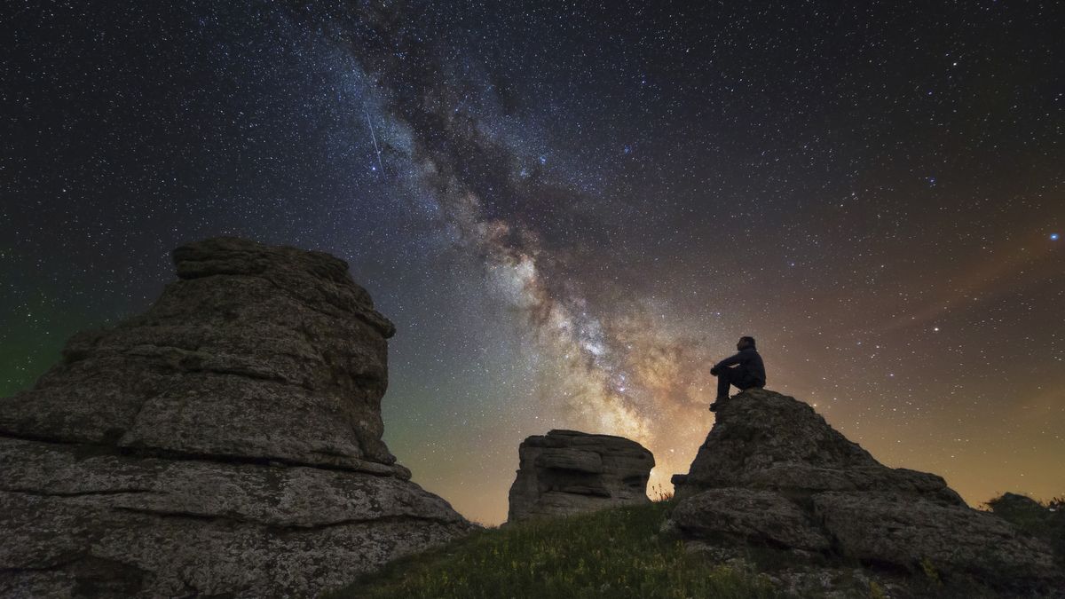 Man sits on top of Demerdzhi mountain under the Milky Way at night in Alushta, Crimea.