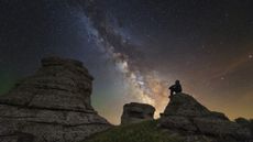 Man sits on top of Demerdzhi mountain under the Milky Way at night in Alushta, Crimea.