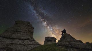 Man sits on top of Demerdzhi mountain under the Milky Way at night in Alushta, Crimea.