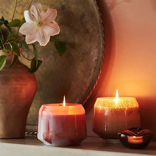 Blushed hued scented candles glowing on mantlepiece, with fresh flowers