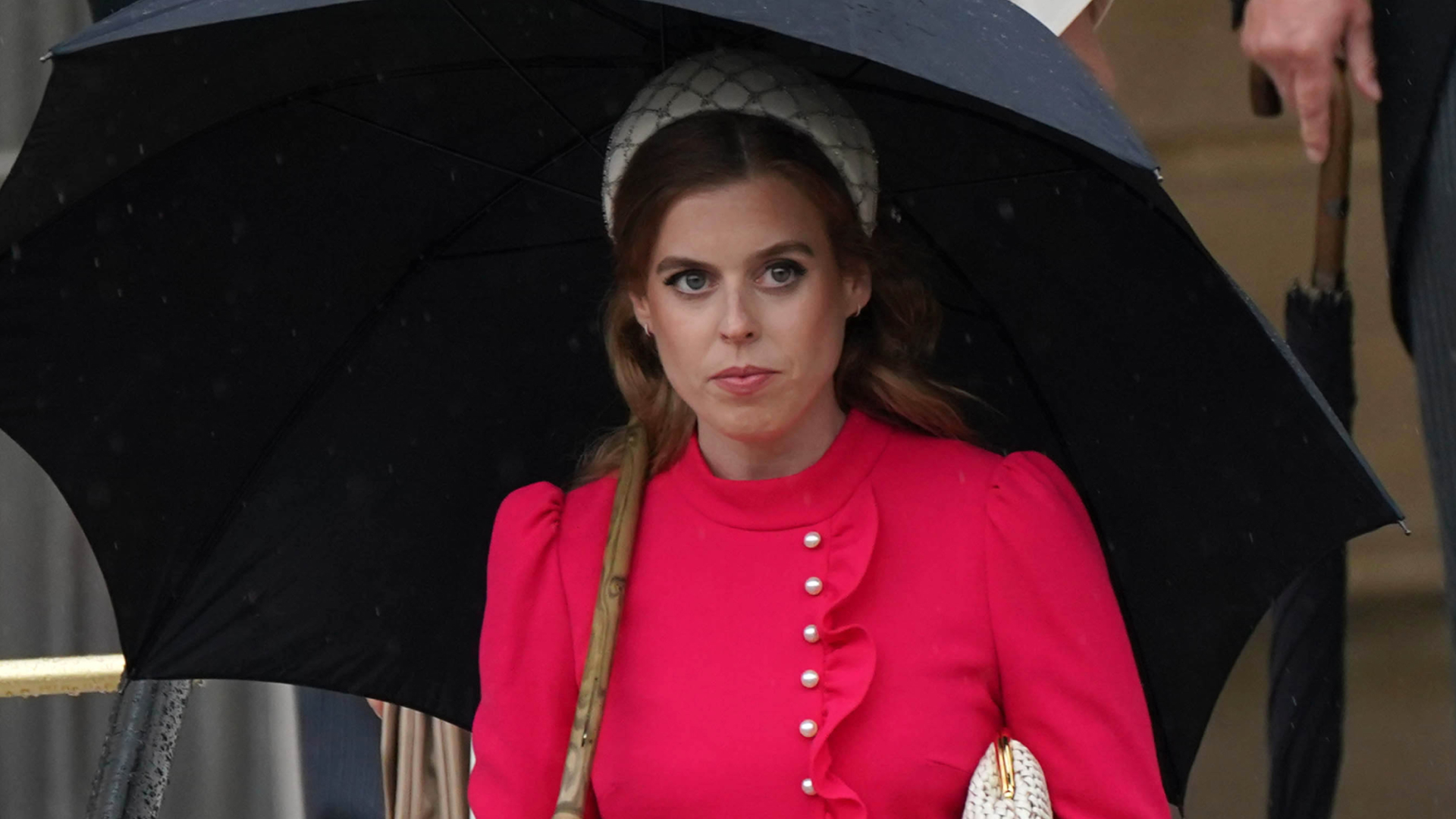 Princess Beatrice wears a red dress and carries a black umbrella while walking in front of sister Princess Eugenie at the Sovereign&#039;s Garden Party at Buckingham Palace on May 21, 2024