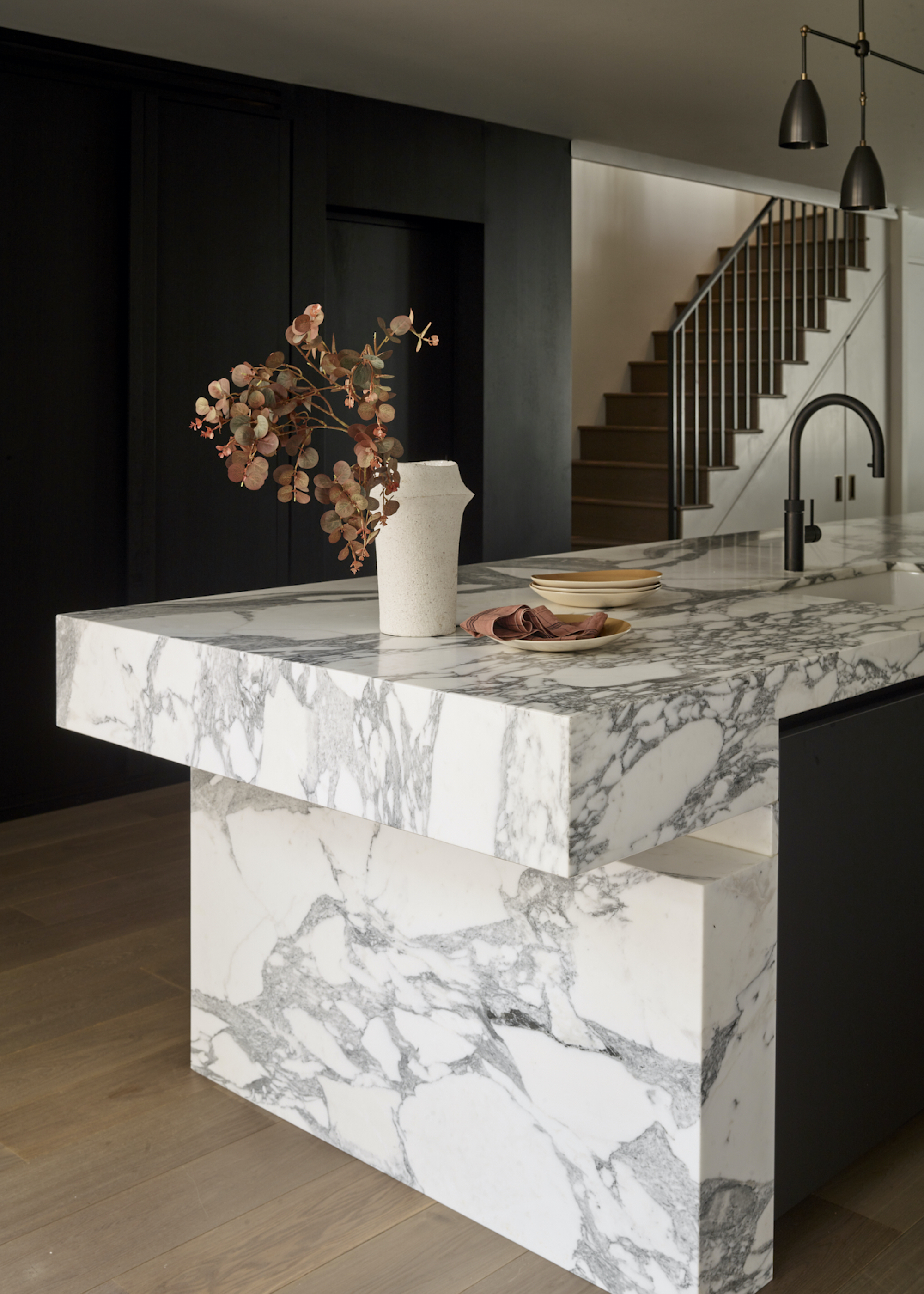 marble island with vase of leaves on top and wood floors