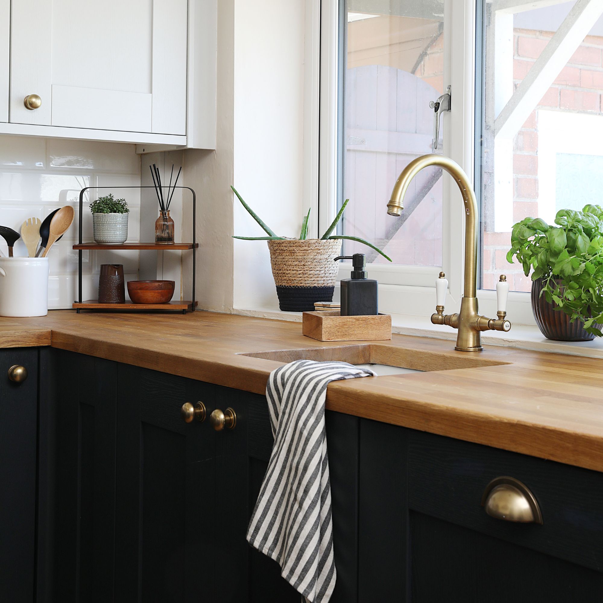 White painted kitchen with wooden worktop and dark black cupboards. There's a gold tap over a sink