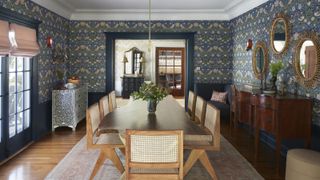 A dining room idea with blue William Morris print wallpaper, large dark wooden sideboard and light wooden dining table with rattan chairs