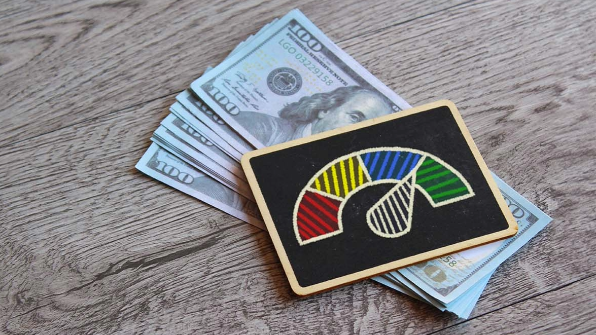 A stack of hundred dollar bills with a card featuring a gauge on top of them.