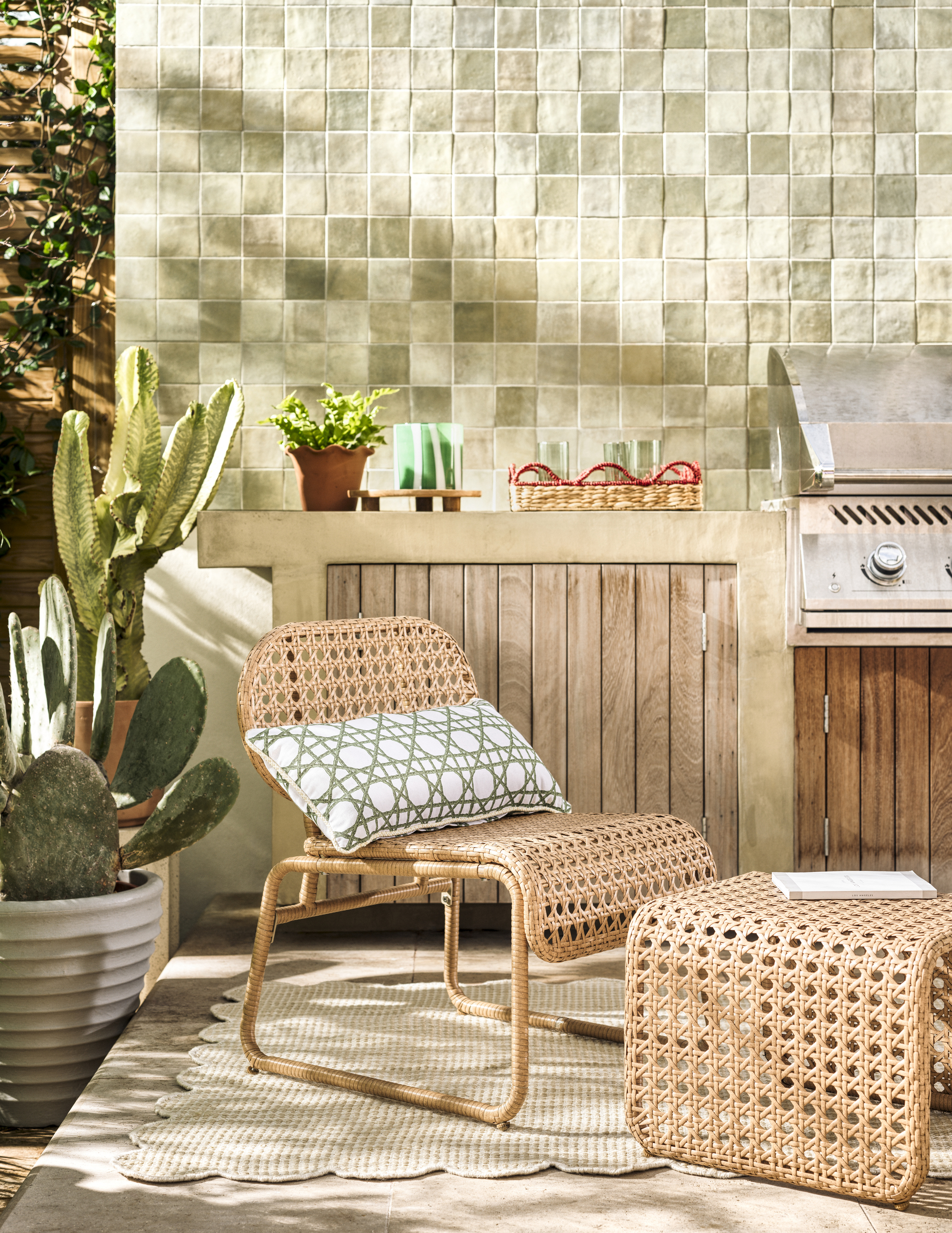 Habitat outdoor chair with ottoman on top of scalloped outdoor rug in front of BBQ and outdoor kitchen with potted cactus