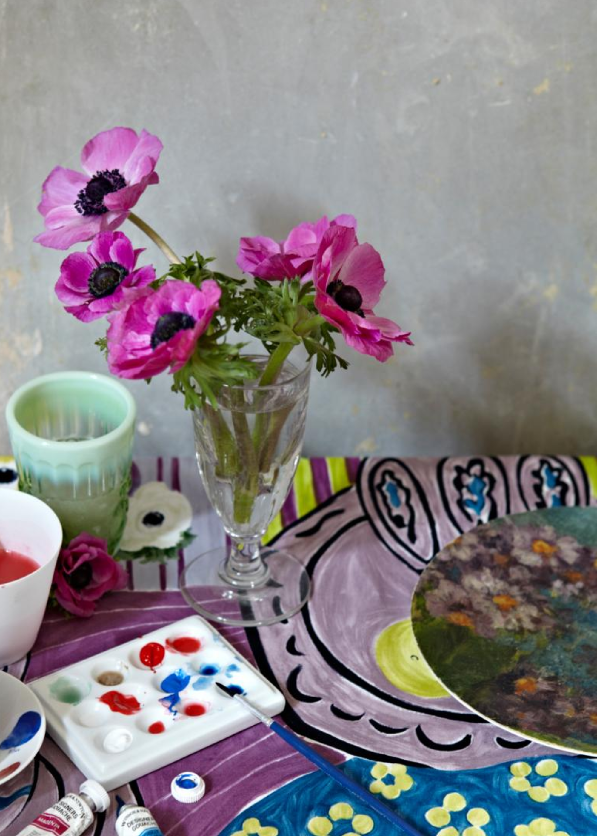 A vase of purple poppies near a paint palette