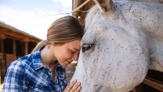 Girl resting head on grey horse's head