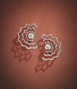 Intricate diamond earrings against a red-pink background