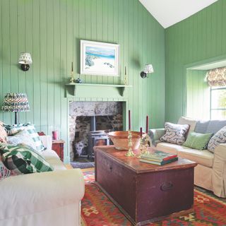 cottage living room with green wood panelled walls and white sofas and chest coffee table