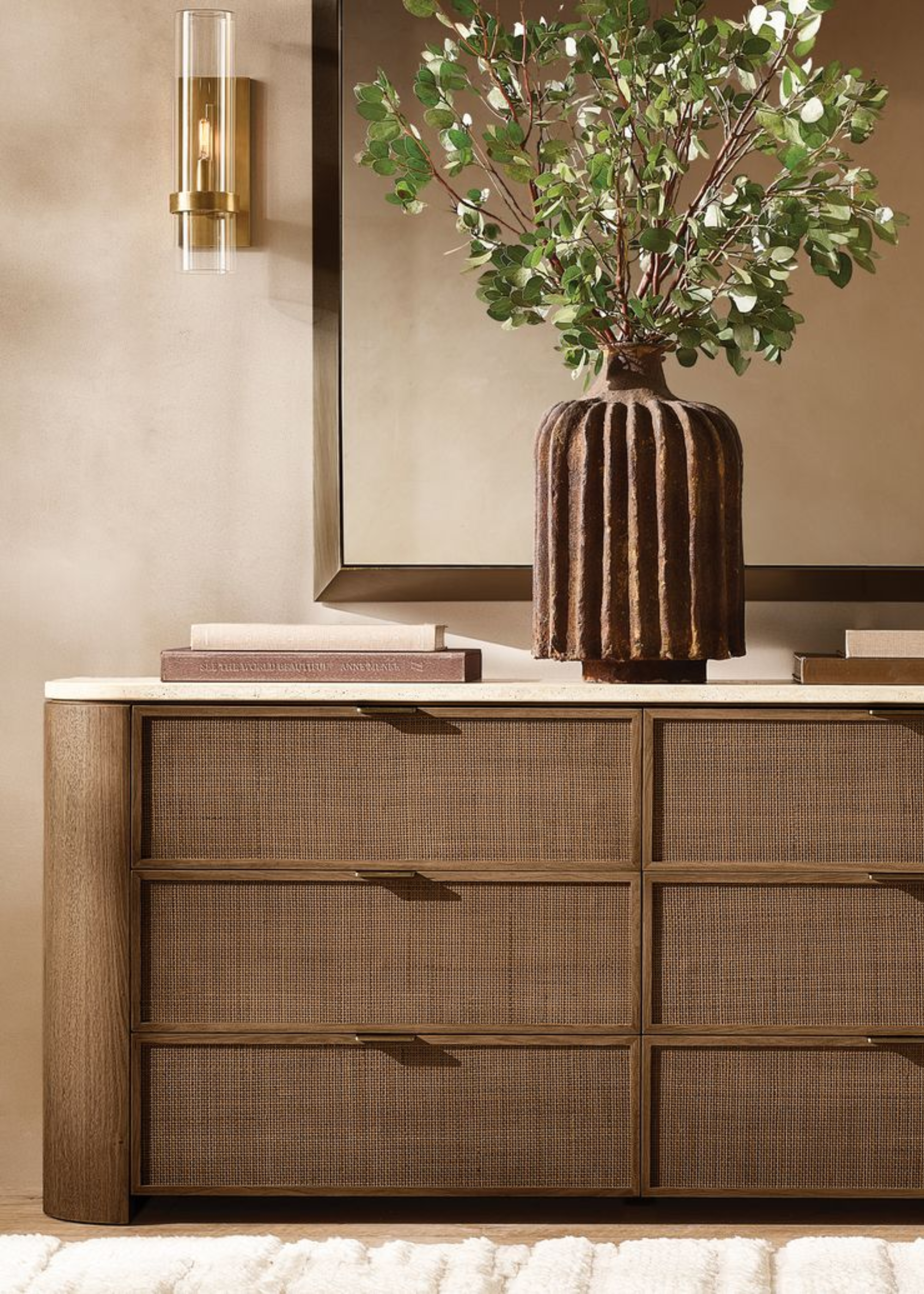 A close-up of a wooden dresser with coffee table books and a vase of stems on top