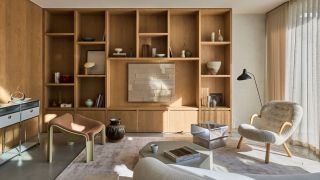 A modern, cozy living room with different textures and furniture pieces. There is a large wooden built-in on the back wall filled with decor, a boucle chair, a metal console, and multiple tables.