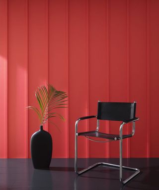 red panelled wall with black chair and black vase with leaf