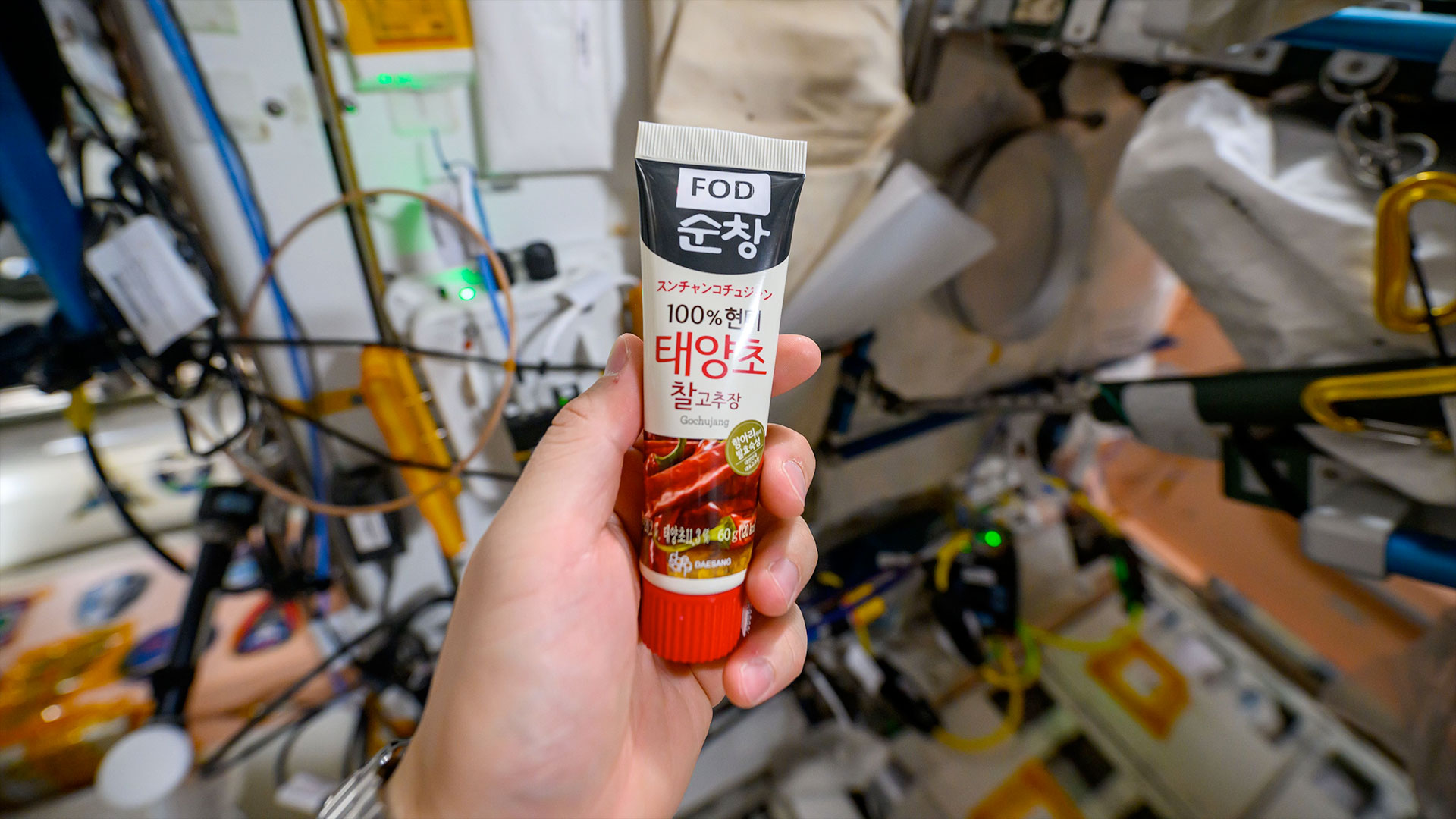 a tube of red pepper paste is held aboard a space station
