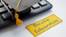 Miniature graduation cap sitting on a keyboard next to a note about taxable scholarships