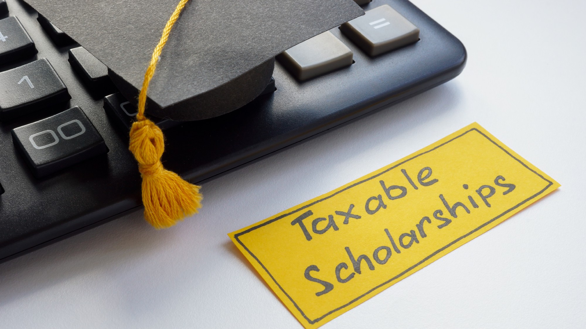 Miniature graduation cap sitting on a keyboard next to a note about taxable scholarships
