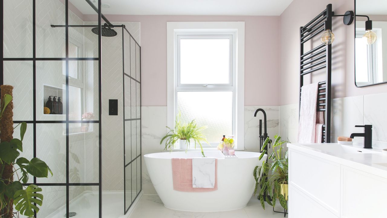 Large bathroom area with pink walls, white marble tiles, a freestanding bath and a large walk-in shower with a black framed shower screen