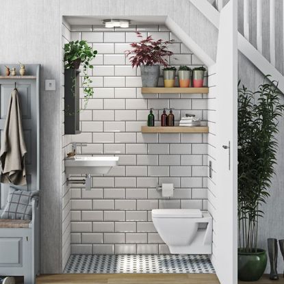 An under stairs toilet with white metro tiles and plants
