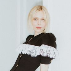 actress ivanna sakhno poses leaning against a wall and wearing a black dress with lace detailing