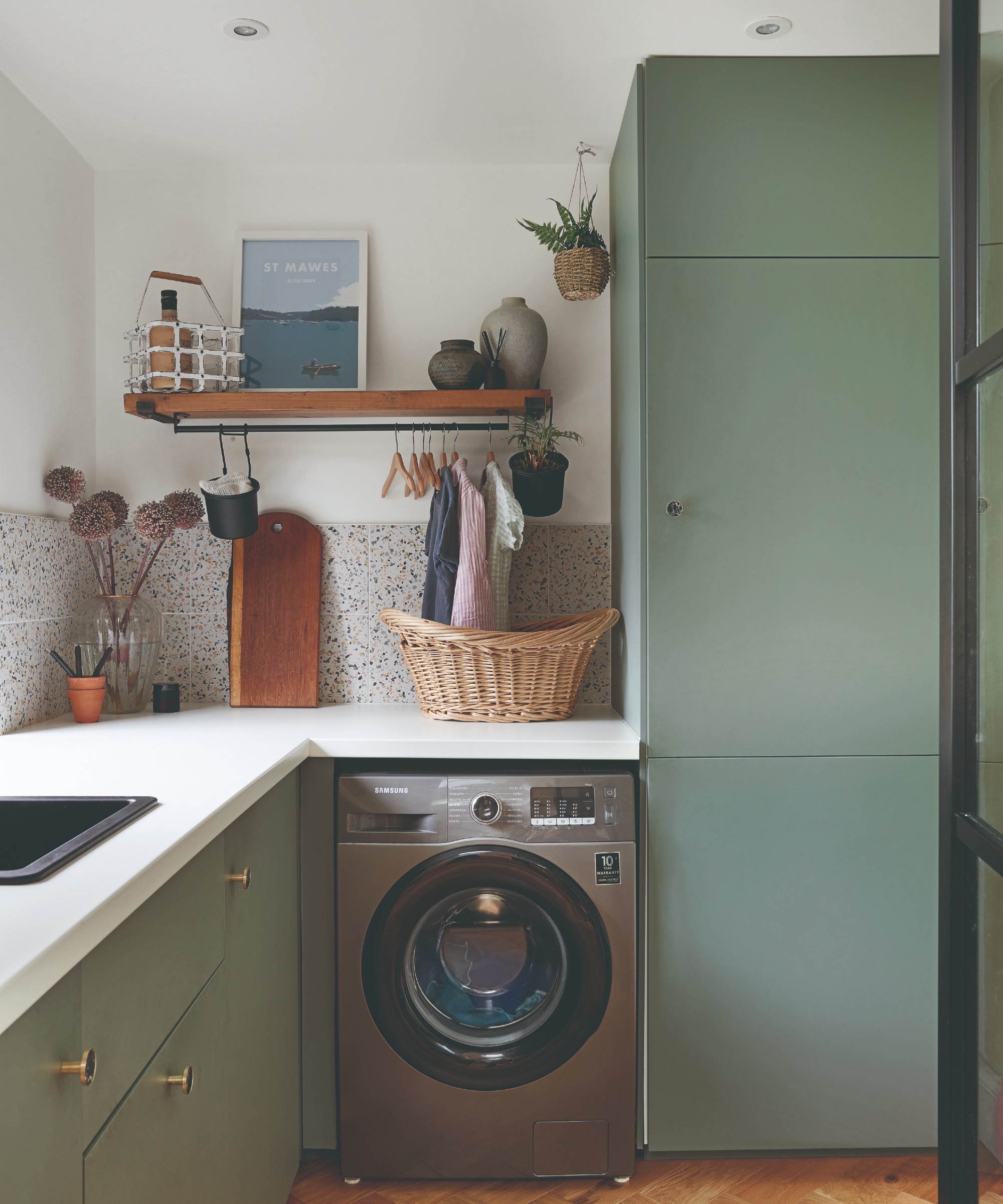 A narrow utility room with green-painted cabinets, white walls and a silver wahing machine