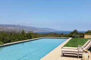outdoor swimming pool with pale stone surround and view of hills and sea beyond
