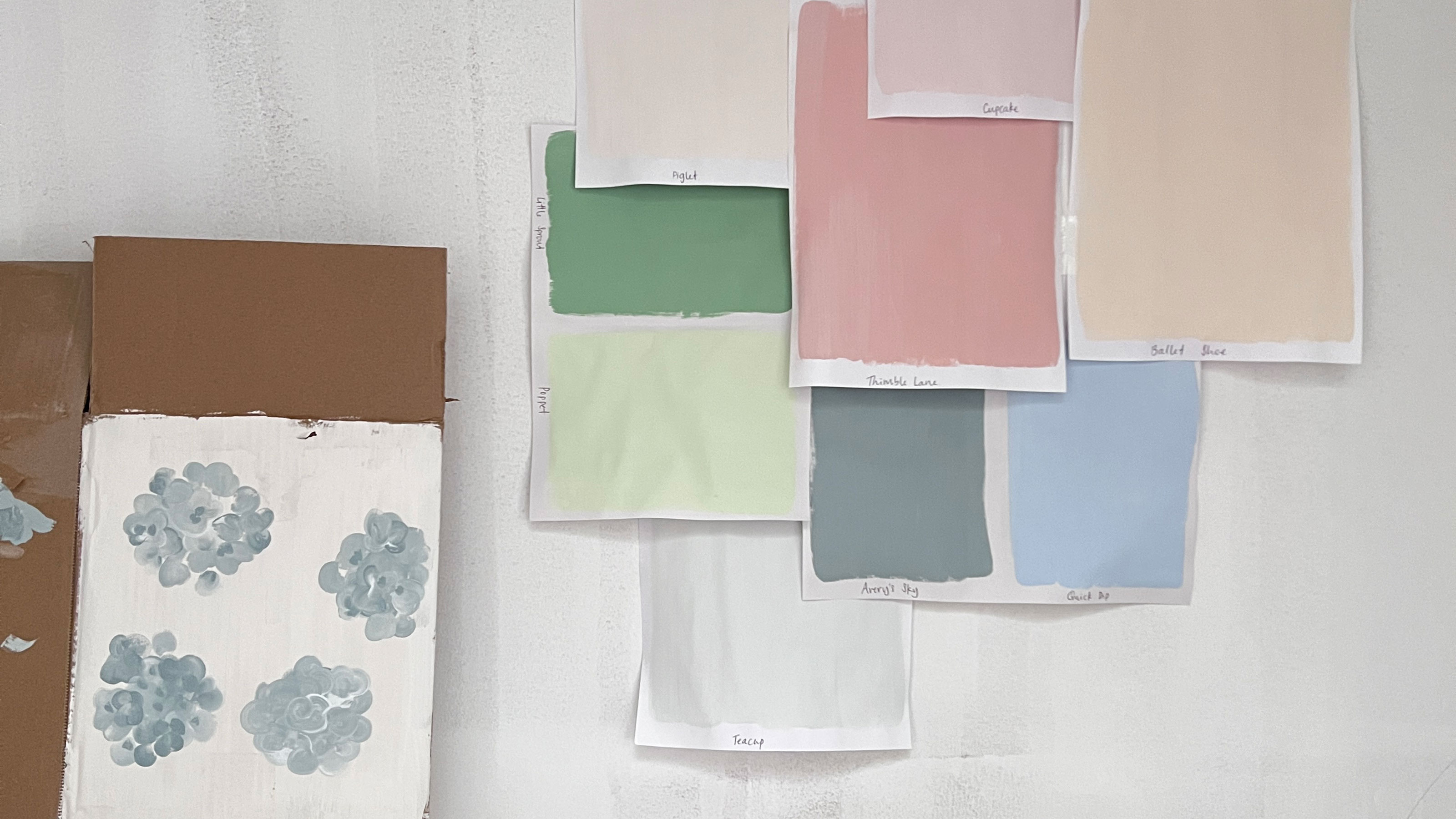 Selection of pink, blue and green paint samples on paper attached to wall 