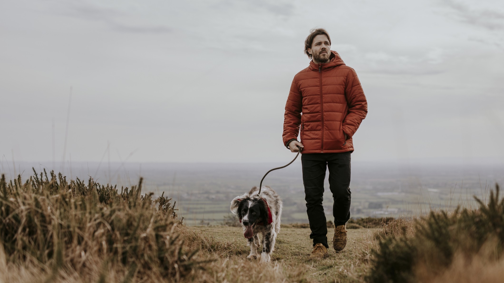 A man walks across a field with a dog on a leash