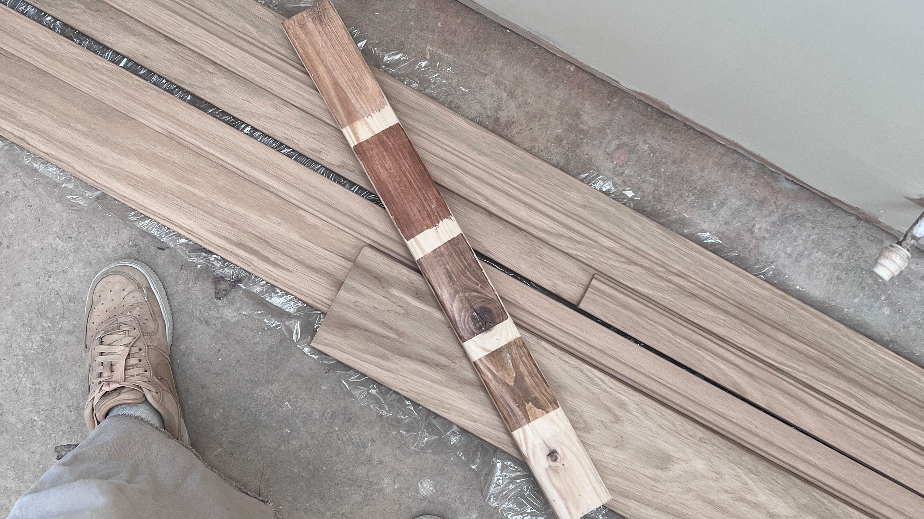 Planks of wood on floor, topped with one plank showing effects of various stains