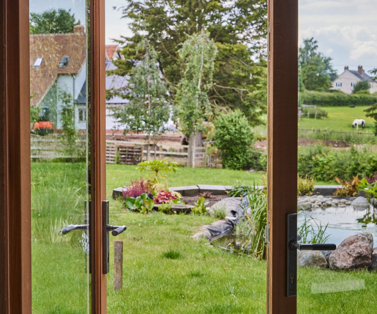 Glass doors which open out into a garden with a lawn and a nature pond