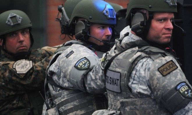 Metro SWAT members hang off the back of a truck as they prepare to search the School and Walnut Street neighborhood for one remaining suspect in Watertown, Mass. 