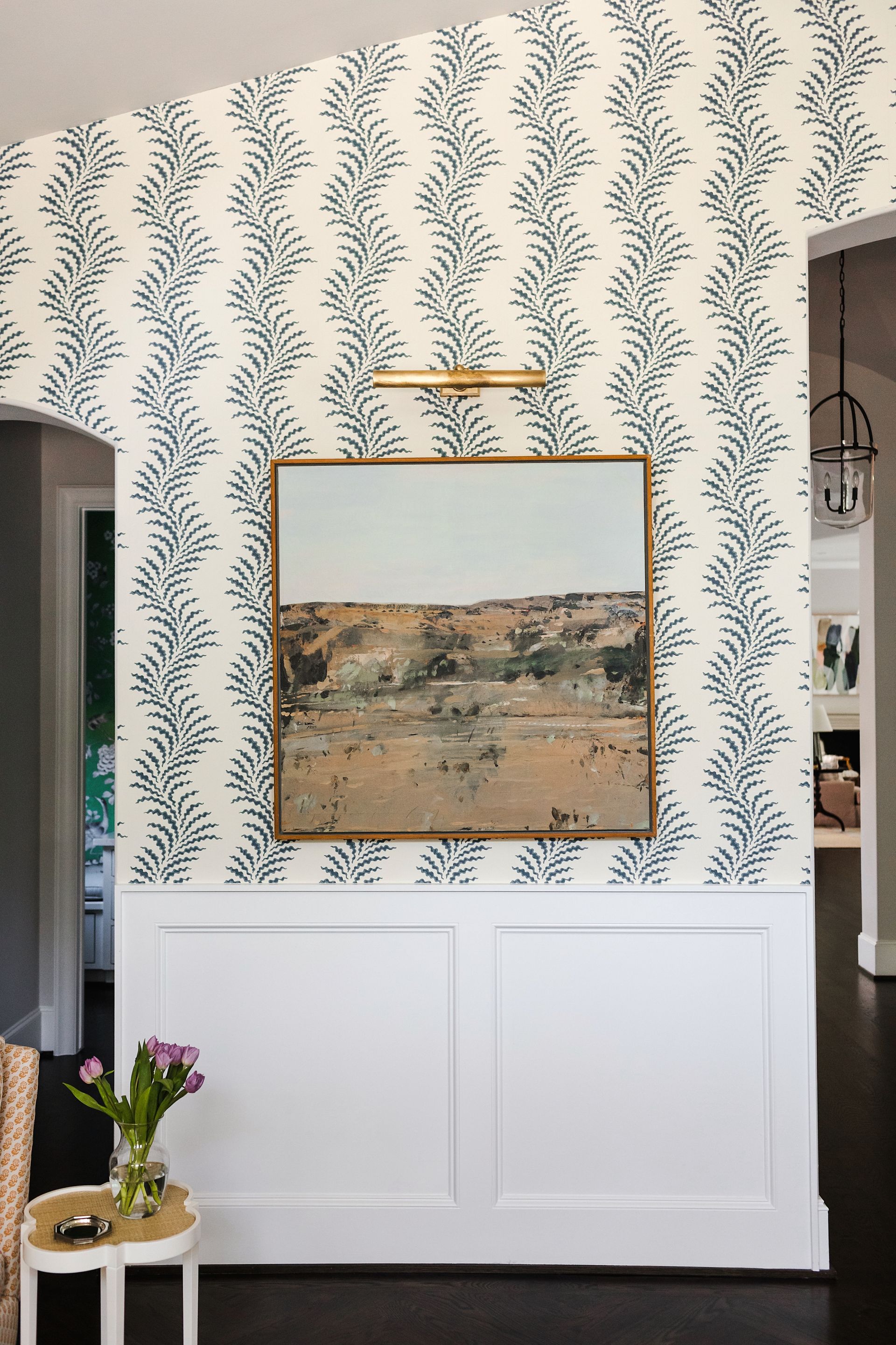 Entryway with patterned wallpaper, artwork with light over and white paneling below