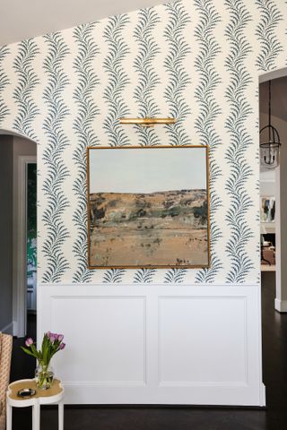 Entryway with patterned wallpaper, artwork with light over and white paneling below