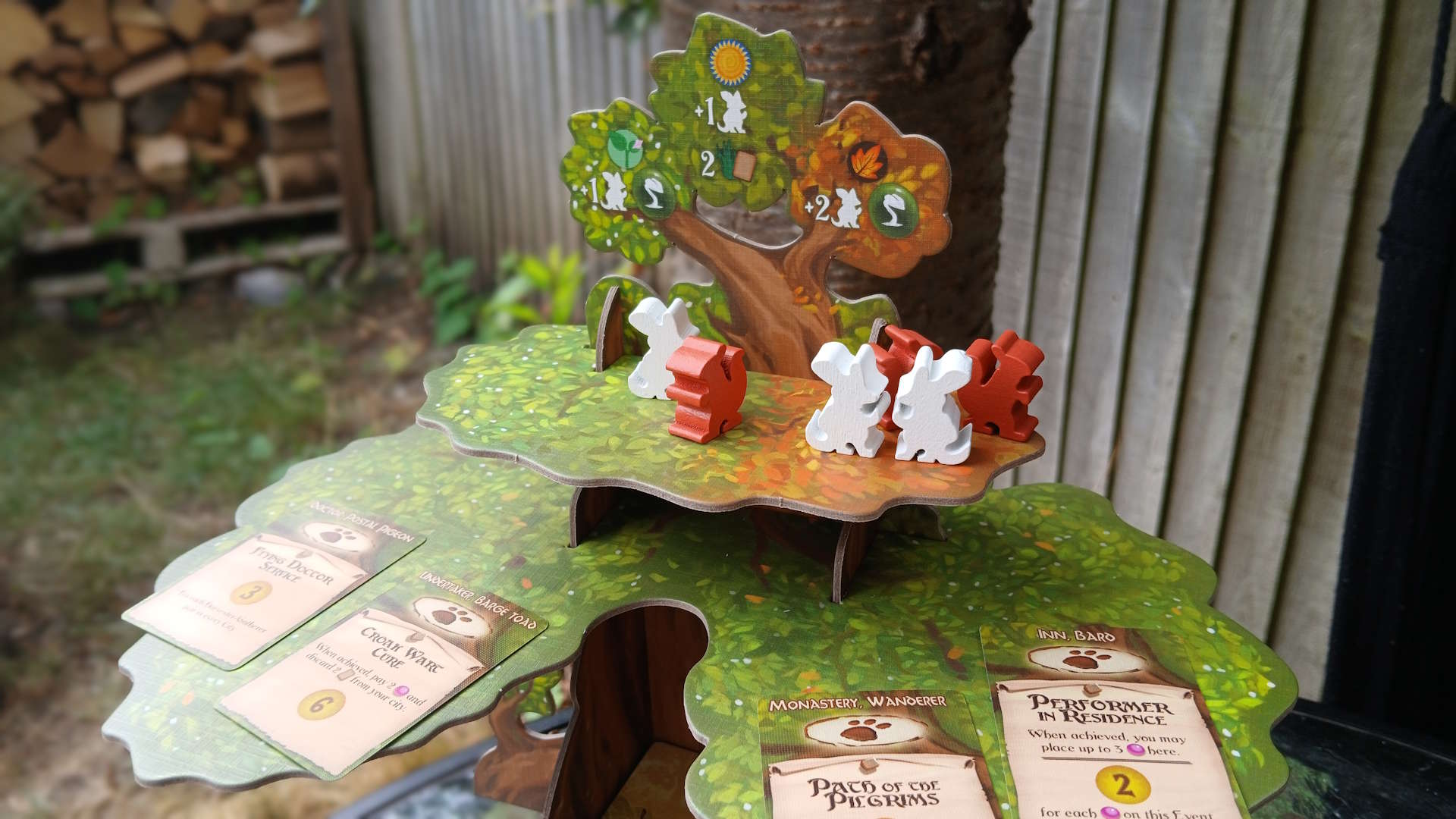 Everdell tree board components laid out in front of a wooden tree and log pile