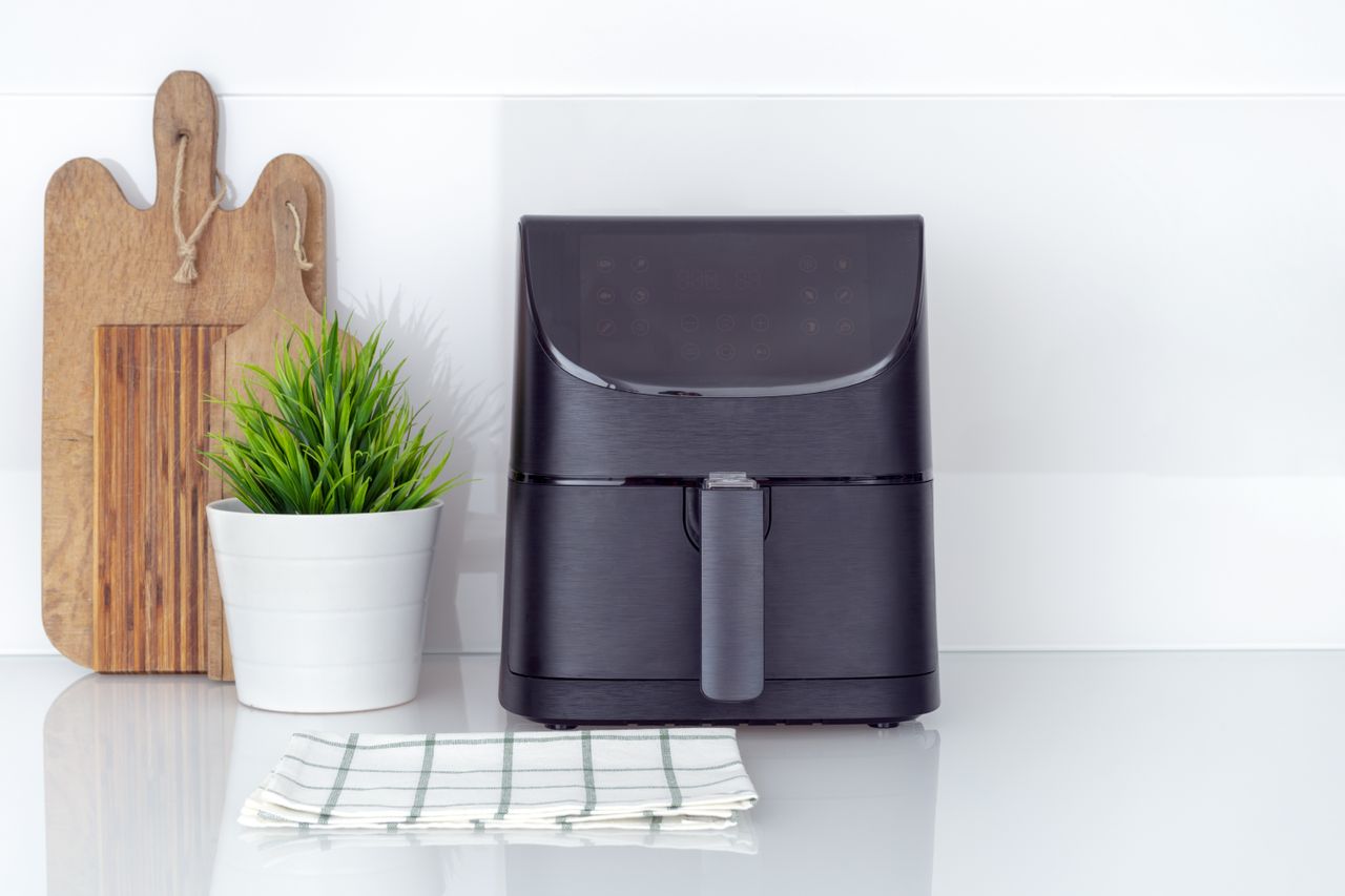 A black air fryer on a white kitchen countertop with a wooden chopping board beside it