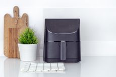 A black air fryer on a white kitchen countertop with a wooden chopping board beside it
