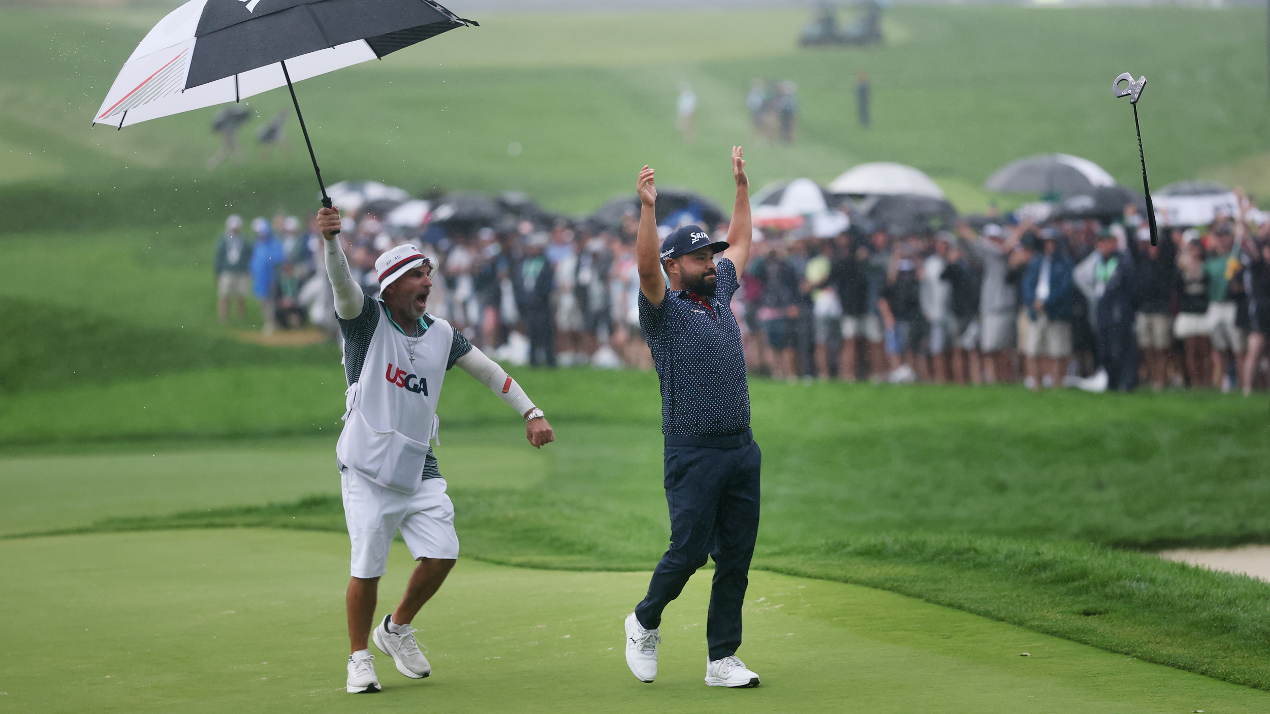 JJ Spaun tosses his putter into the air after holing the winning putt at the 2025 US Open while his caddie celebrates while holding an umbrella behind