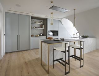 A kitchen peninsula with a black worktop and gold legs with stylish cream and black bar stools under two pendant lamps