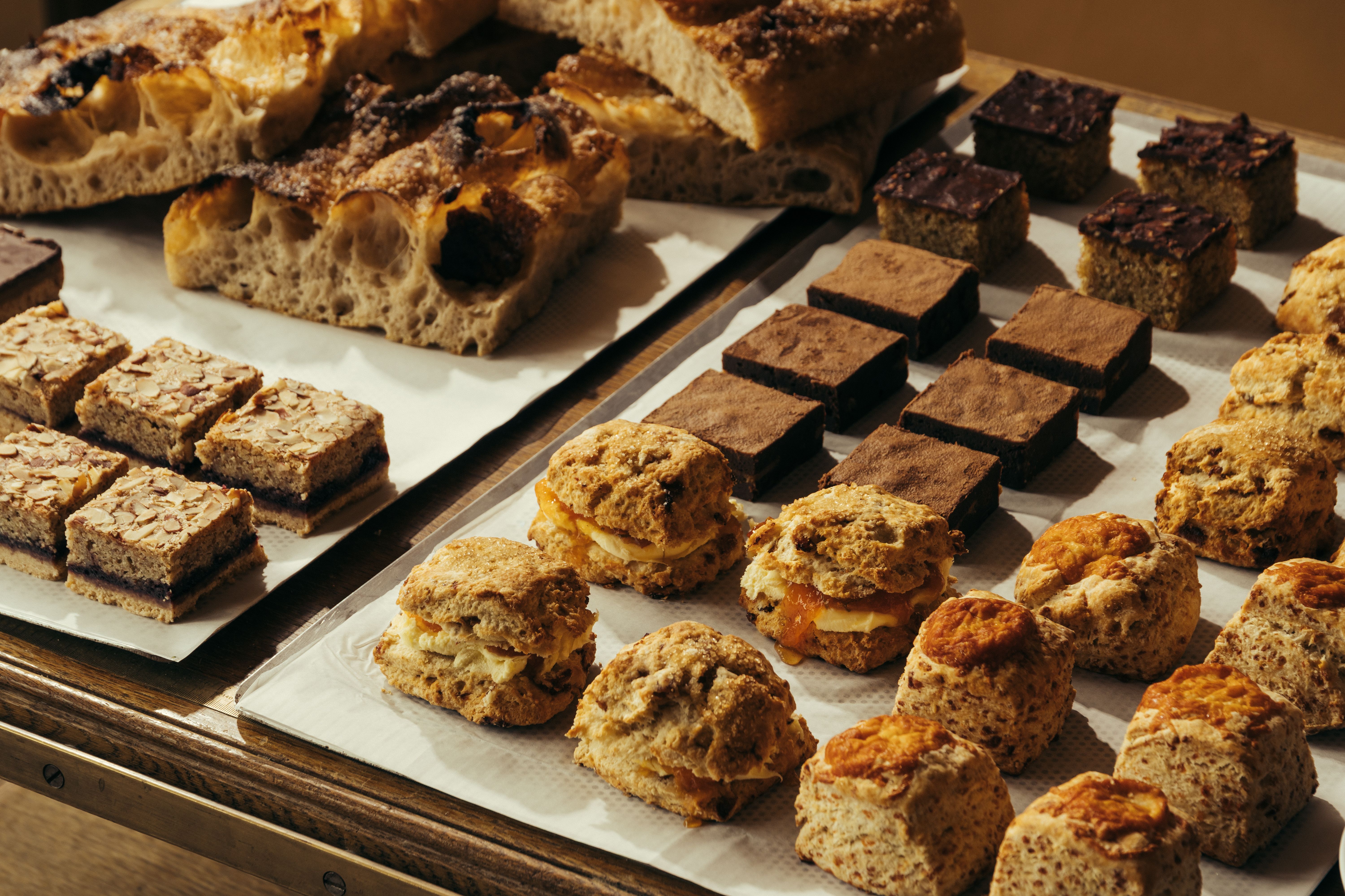 An ochre-painted cafe and bakery filled with wooden furnishings and industrial pendant lighting, along with lots of freshly baked goods, beautifully plated food, and coffee cups.