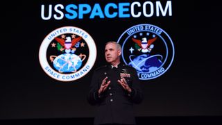 a man in a black military dress uniform speaks on a stage in front of an image of earth seen from space