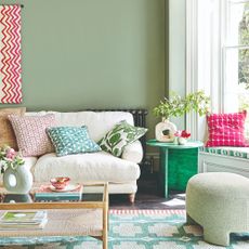 A sage green-painted living room with a matching pouffe and a cream sofa